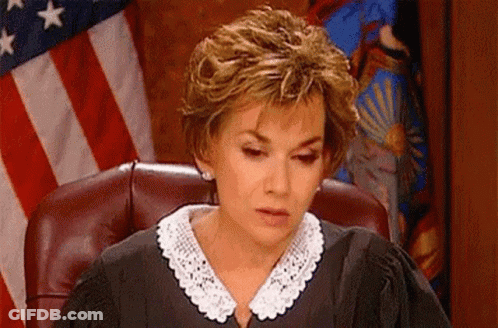 A Woman In A Judge 'S Robe Is Sitting In A Courtroom In Front Of An American Flag . GIF