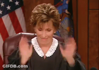 A Woman In A Judge 'S Robe Is Sitting In Front Of An American Flag And Clapping Her Hands . GIF