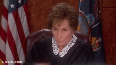 A Woman In A Judge 'S Robe Is Sitting In Front Of An American Flag In A Courtroom . GIF