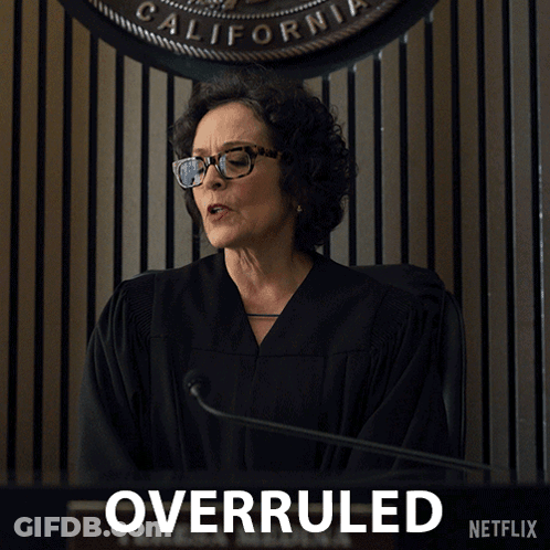 A Woman In A Judge 'S Robe Stands In Front Of A Sign That Says Overruled On It GIF