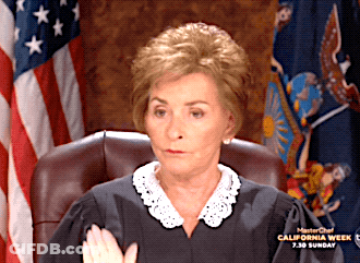 A Woman In A Judge 'S Robes Is Sitting In Front Of An American Flag GIF