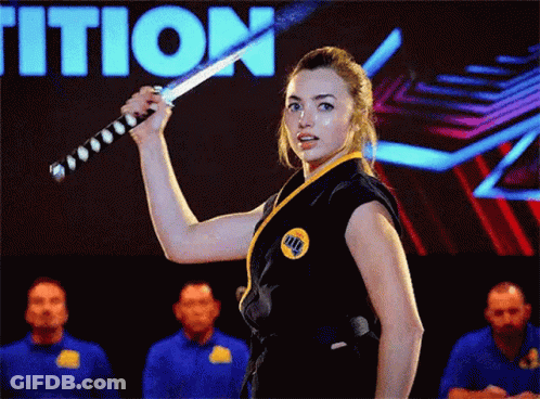A Woman In A Karate Uniform Is Holding A Sword In Front Of A Group Of People . GIF