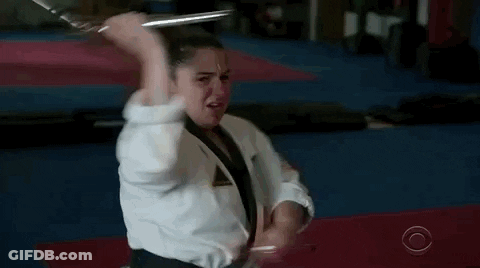 A Woman In A Karate Uniform Is Holding A Sword In Her Hand . GIF