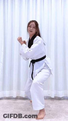 A Woman In A Karate Uniform Is Jumping In The Air While Holding A Sword . GIF