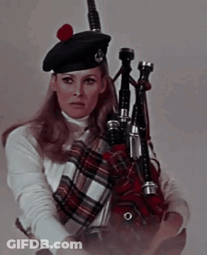 A Woman In A Kilt Is Holding A Bagpipe In Her Hand . GIF