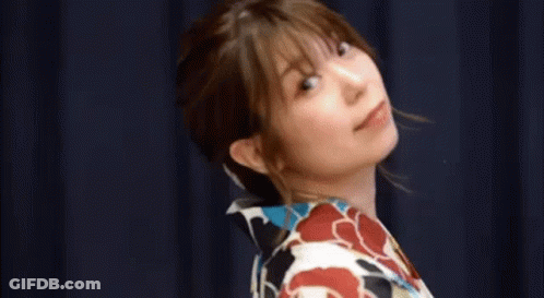 A Woman In A Kimono Is Standing In Front Of A Blue Curtain With Her Eyes Closed . GIF