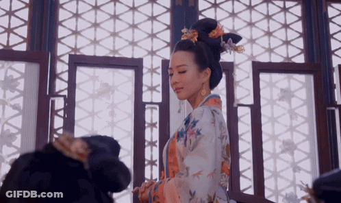A Woman In A Kimono With Flowers In Her Hair Is Standing In Front Of A Window GIF