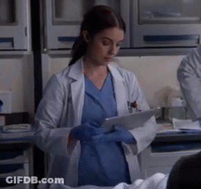 A Woman In A Lab Coat And Blue Scrubs Is Using A Tablet GIF