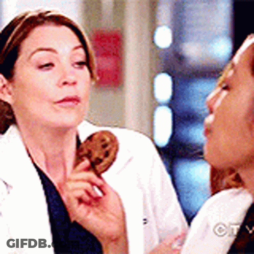 A Woman In A Lab Coat Is Holding A Cookie In Her Hand While Another Woman Looks On . GIF