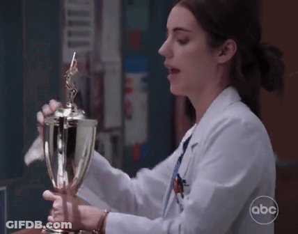 A Woman In A Lab Coat Is Holding A Trophy With Abc Written On The Bottom GIF