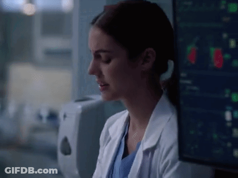 A Woman In A Lab Coat Is Sitting In Front Of A Computer Monitor In A Hospital Room . GIF