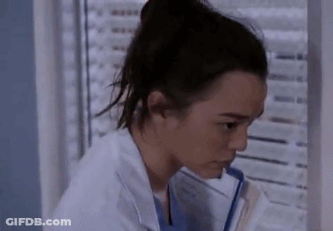 A Woman In A Lab Coat Is Sitting In Front Of A Window Holding A Clipboard . GIF