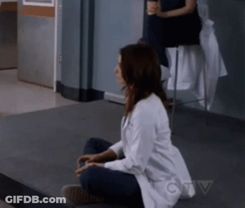A Woman In A Lab Coat Is Sitting On The Floor In Front Of A Ctv Sign GIF