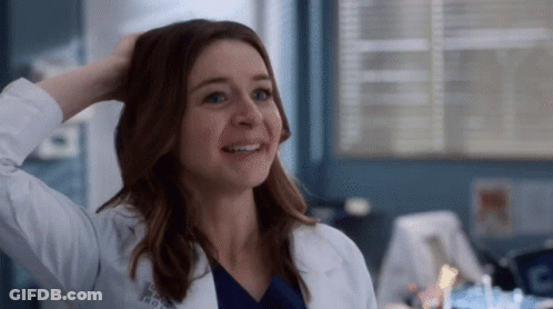A Woman In A Lab Coat Is Smiling While Holding Her Hair . GIF