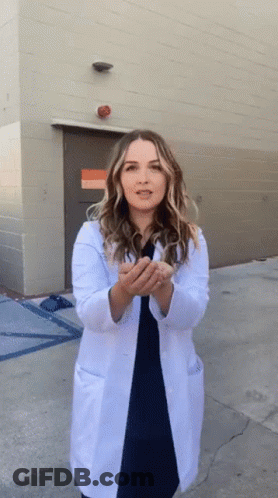A Woman In A Lab Coat Is Standing Outside A Building GIF