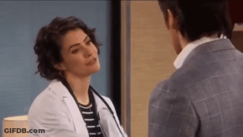 A Woman In A Lab Coat Is Talking To A Man In A Suit In A Hospital Room . GIF