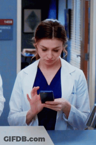 A Woman In A Lab Coat Is Using A Cell Phone GIF