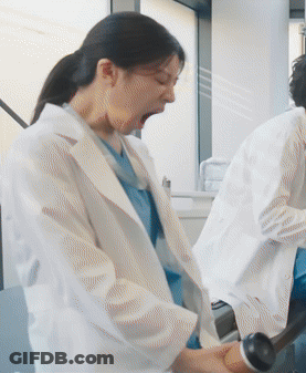 A Woman In A Lab Coat Is Yawning While A Man In A Lab Coat Is Using A Machine . GIF