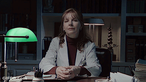 A Woman In A Lab Coat Sits At A Desk GIF