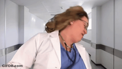A Woman In A Lab Coat With A Stethoscope Around Her Neck Is Standing In A Hospital Hallway . GIF