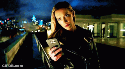 A Woman In A Leather Jacket Holds A Cell Phone With The Letter O On It GIF