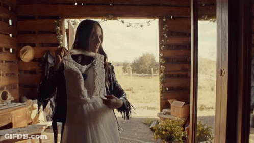 A Woman In A Leather Jacket Holds A White Dress GIF