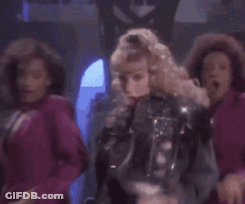 A Woman In A Leather Jacket Is Dancing In Front Of A Group Of Dancers In Pink Dresses . GIF