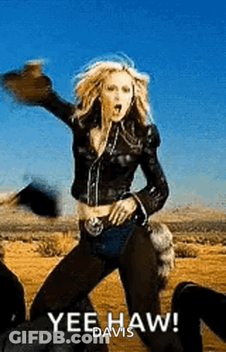 A Woman In A Leather Jacket Is Dancing In The Desert While Wearing A Hat . GIF