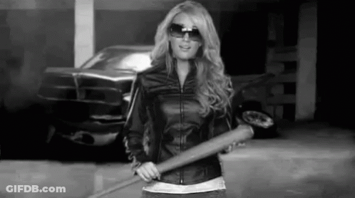 A Woman In A Leather Jacket Is Holding A Baseball Bat In A Parking Lot . GIF