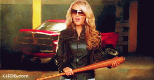 A Woman In A Leather Jacket Is Holding A Baseball Bat In Front Of A Red Truck GIF