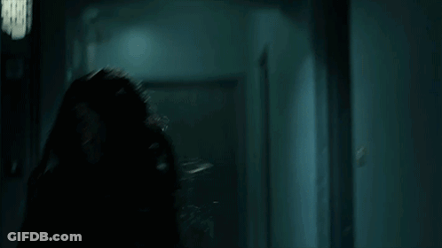 A Woman In A Leather Jacket Is Running Through A Dark Hallway In A Dark Room . GIF