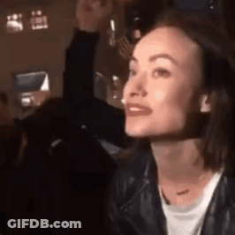 A Woman In A Leather Jacket Is Sitting At A Table In A Dark Room . GIF