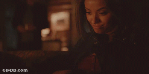 A Woman In A Leather Jacket Is Smiling And Looking At Something GIF