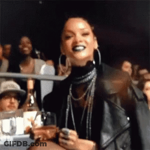 A Woman In A Leather Jacket Is Standing In A Crowd Holding A Glass Of Wine And A Cell Phone . GIF