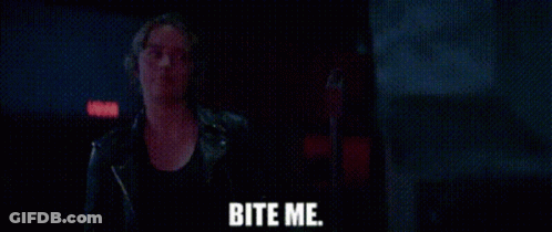 A Woman In A Leather Jacket Is Standing In A Dark Room With The Words Bite Me Written On The Screen . GIF