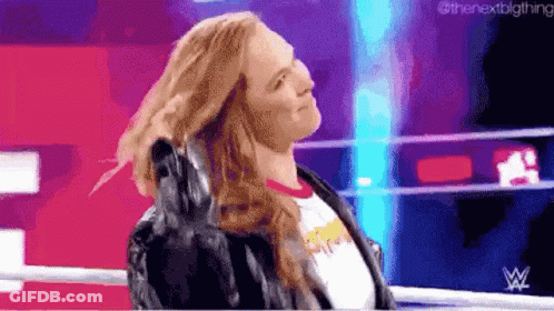 A Woman In A Leather Jacket Is Standing In A Wrestling Ring Holding Her Hair . GIF