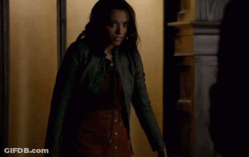 A Woman In A Leather Jacket Is Standing In Front Of A Door . GIF