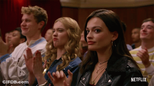 A Woman In A Leather Jacket Sits In A Crowd Of People Applauding GIF