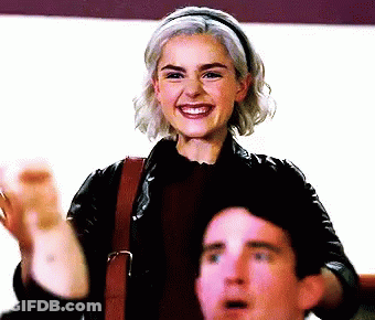 A Woman In A Leather Jacket Smiles While A Man Looks On GIF