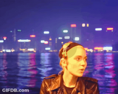 A Woman In A Leather Jacket Stands In Front Of A City Skyline At Night GIF