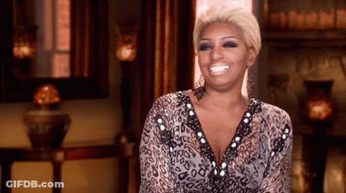 A Woman In A Leopard Print Dress Is Smiling In Front Of A Fireplace GIF
