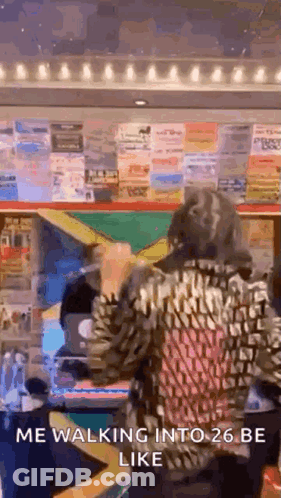 A Woman In A Leopard Print Jacket Is Walking Into A 26 Be Like Sign . GIF