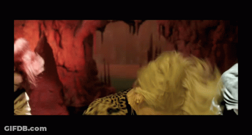 A Woman In A Leopard Print Shirt Is Dancing In Front Of A Red Wall GIF
