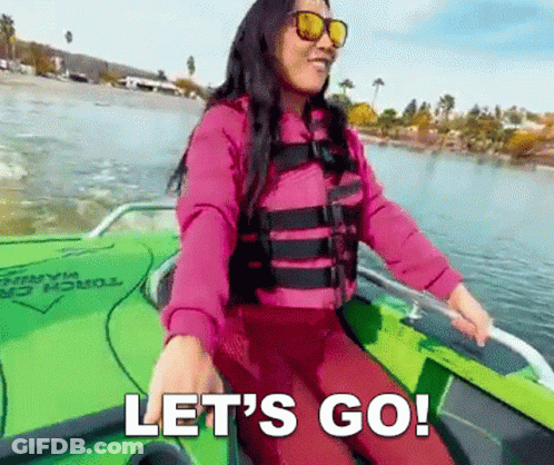 A Woman In A Life Jacket And Sunglasses Is Sitting In A Boat On A Lake And Says Let 'S Go . GIF