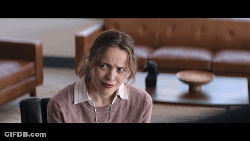 A Woman In A Living Room With A Couch And A Coffee Table GIF
