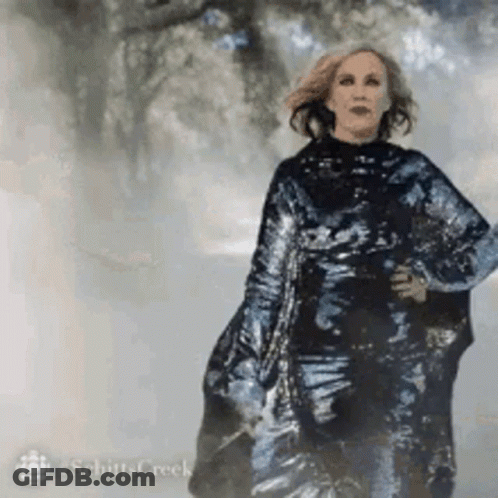 A Woman In A Long Black Dress Is Walking Down A Foggy Street . GIF