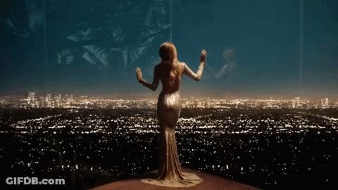A Woman In A Long Dress Is Standing In Front Of A City Skyline At Night . GIF