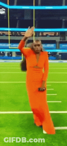 A Woman In A Long Orange Dress Is Dancing On A Football Field GIF