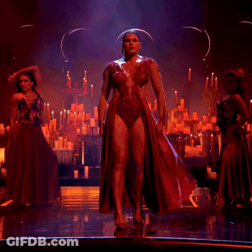 A Woman In A Long Red Dress Is Dancing On A Stage GIF
