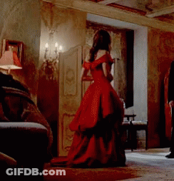A Woman In A Long Red Dress Is Standing In A Room GIF
